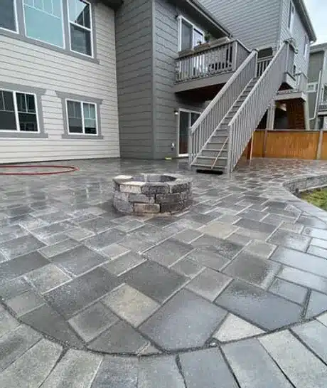 Stacked stone fire pit on a large format gray paver patio behind a two story home by Blackpine Hardscapes